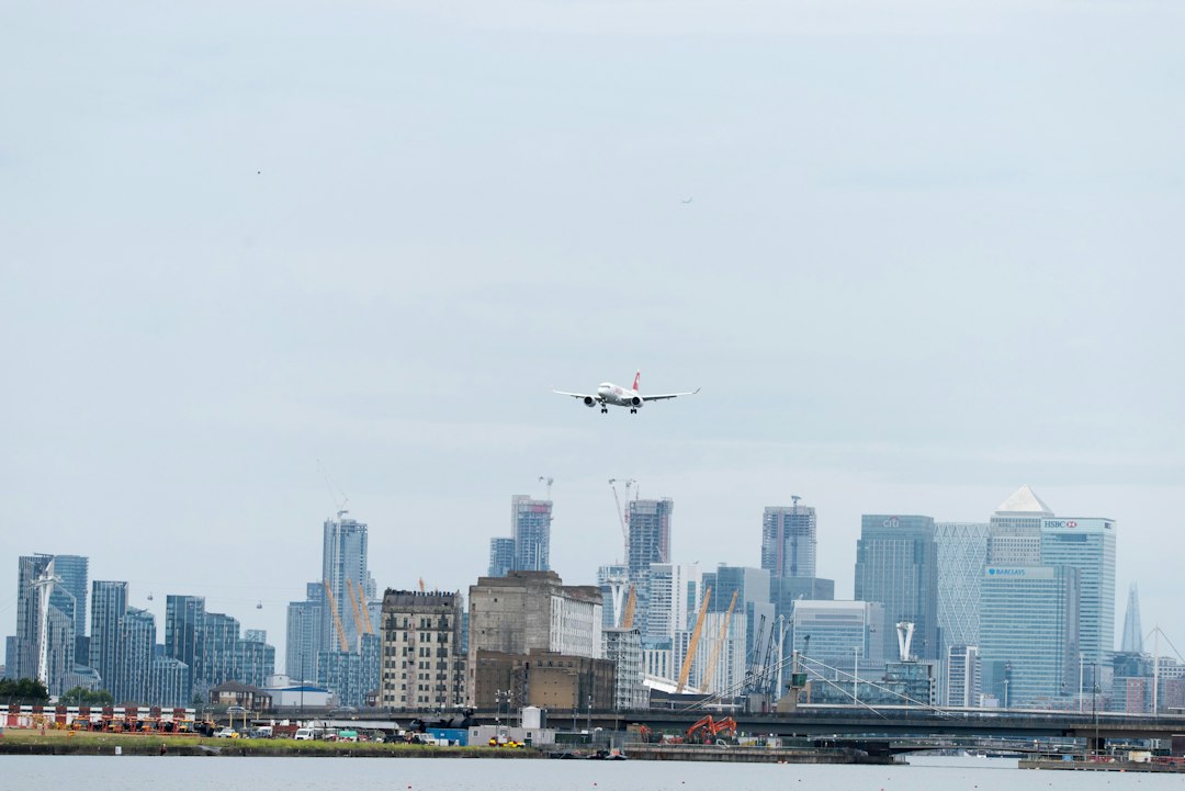 Airliner on low final approach over a waterfront city skyline, showing how close arriving traffic flies to the ground near a busy airport
