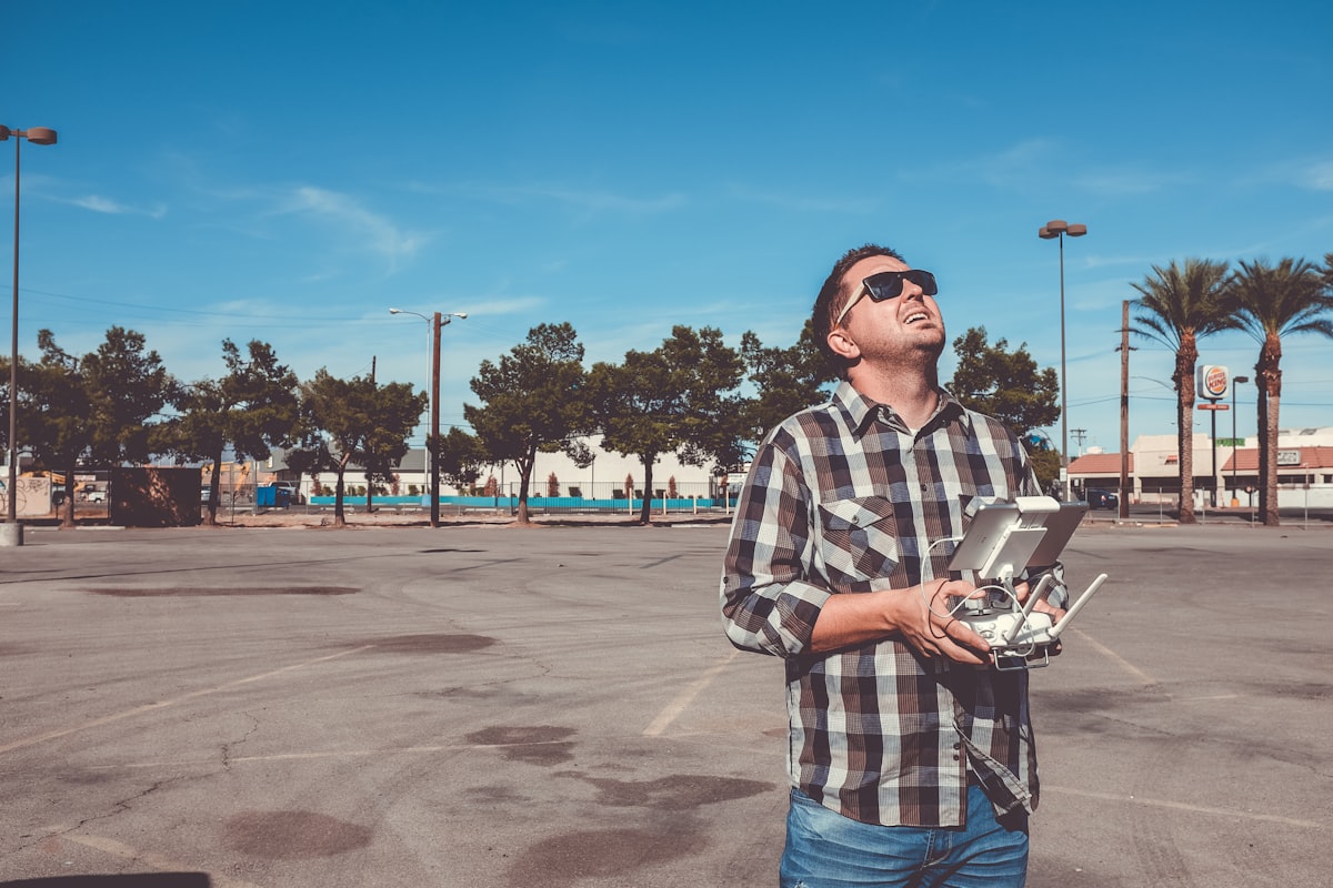 Drone pilot holding a remote controller and looking up at the sky in an open commercial area