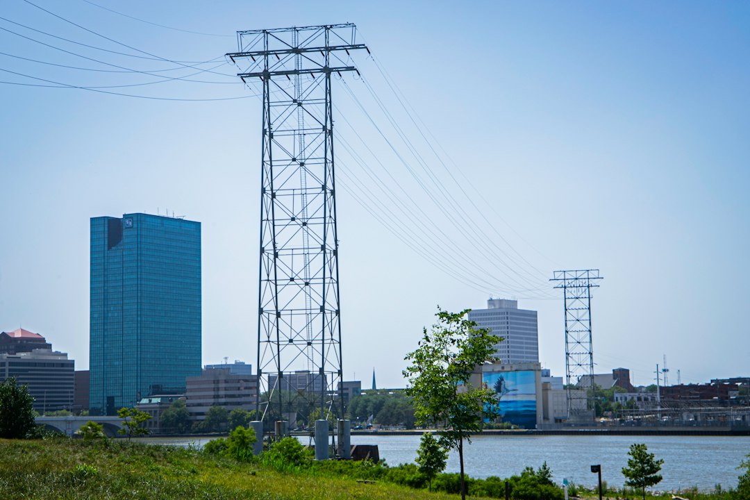 Steel electrical transmission tower and power lines by a river, the kind of utility asset a DJI Matrice 30T thermal drone inspects