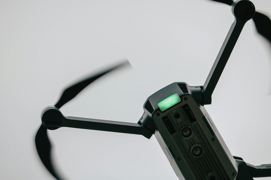 Quadcopter in flight viewed from below with spinning propellers against a pale sky, illustrating drone as a service operations