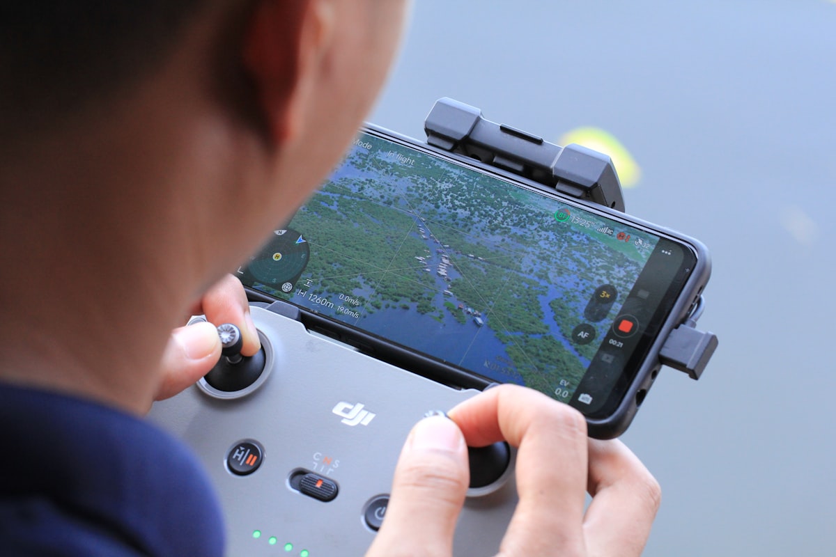 Drone operator using a DJI controller with aerial map view on screen during a commercial mission