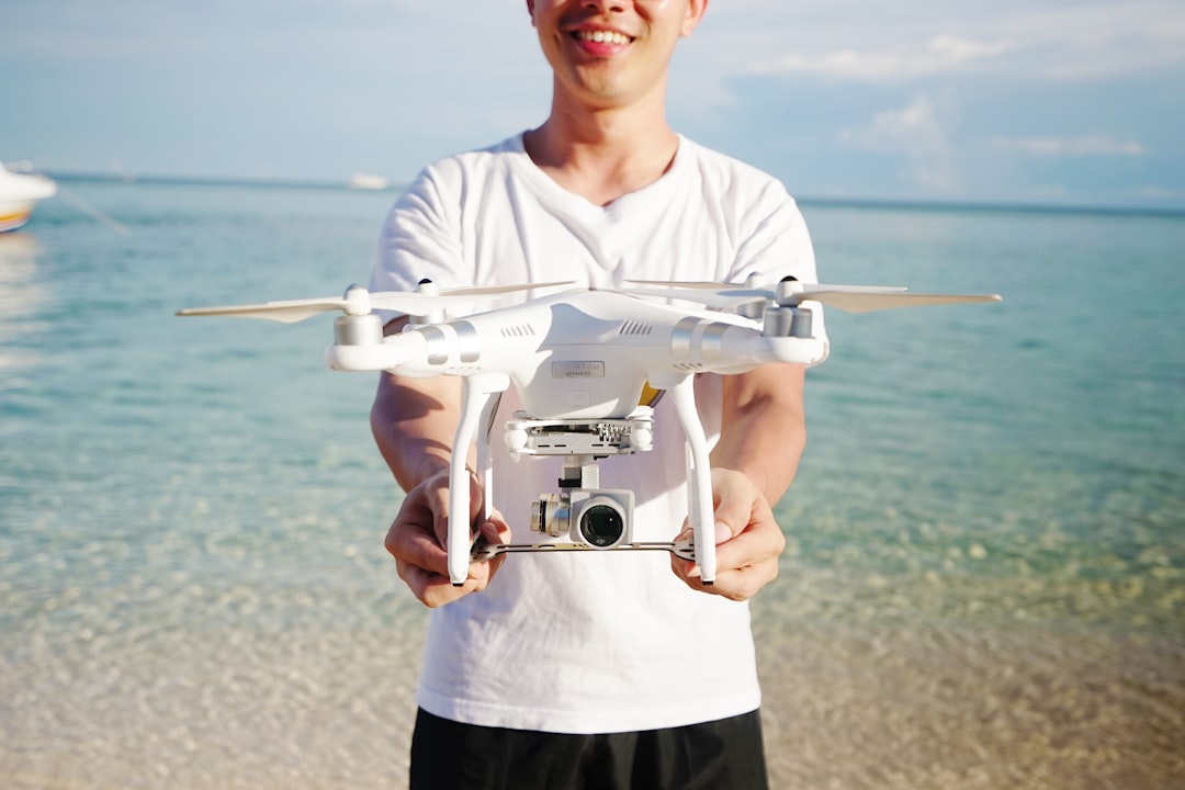 Drone photographer holding a white DJI camera drone at a coastal location before a commercial shoot