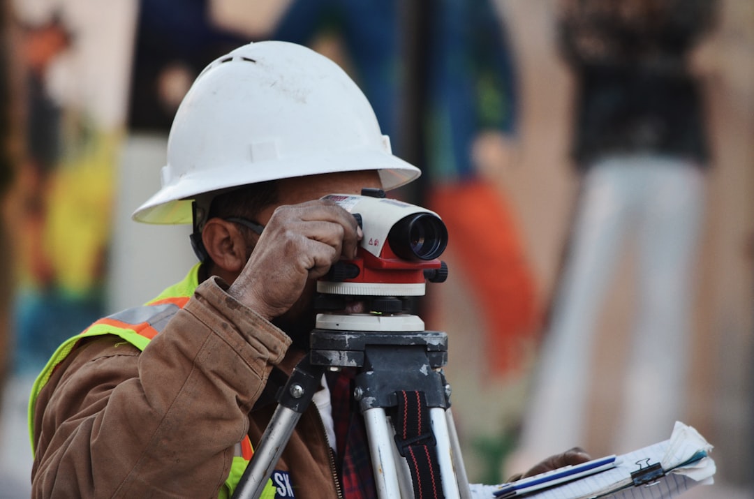 Land surveyor sighting through a tripod-mounted level on a job site, the ground control work drone surveying software depends on