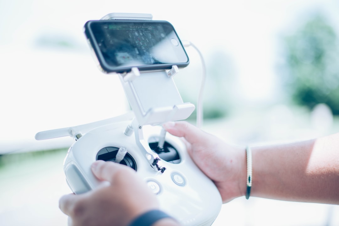 Drone pilot holding a controller with a smartphone running a drone tracking app showing live flight position