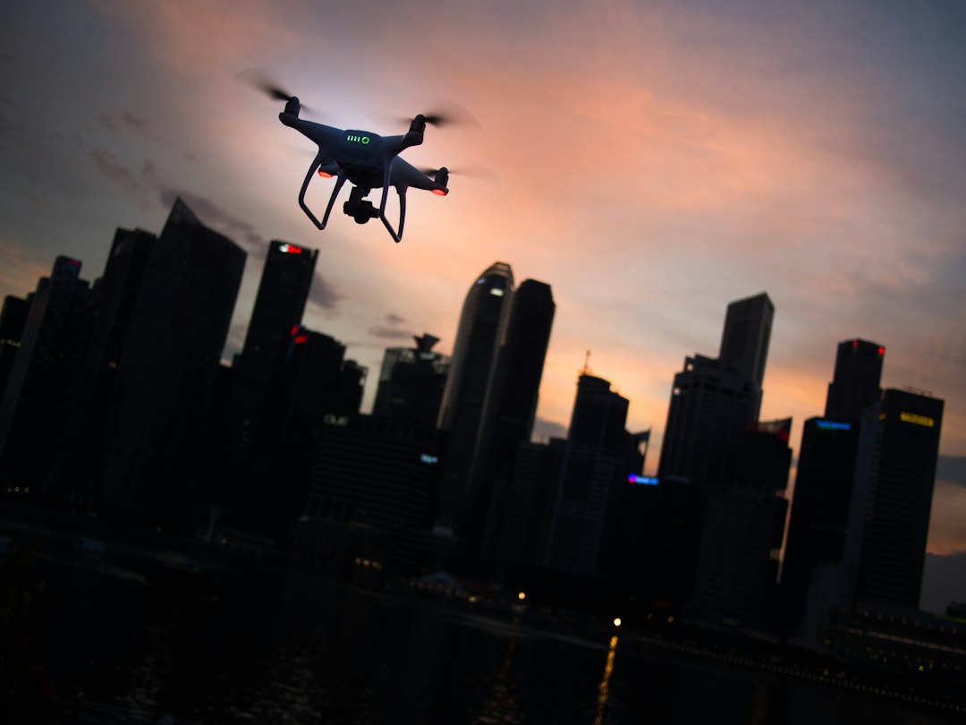 Quadcopter drone silhouetted over a city skyline at dusk, illustrating urban drone operations managed with software like DroneSense